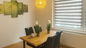 A dining area with a wooden table, black chairs, a yellow pendant light, and a window with blinds. - C&V: 5 PP- 3 rooms- central+WLAN+box spring bed (Kaiserslautern)
