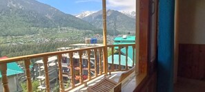 A balcony with a view of a mountainous landscape, a green-roofed building, and a blue wall. - Trippeaze stays (Manali)