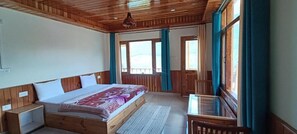 A bedroom with a wooden bed, a small desk, and a window with curtains. - Trippeaze stays (Manali)