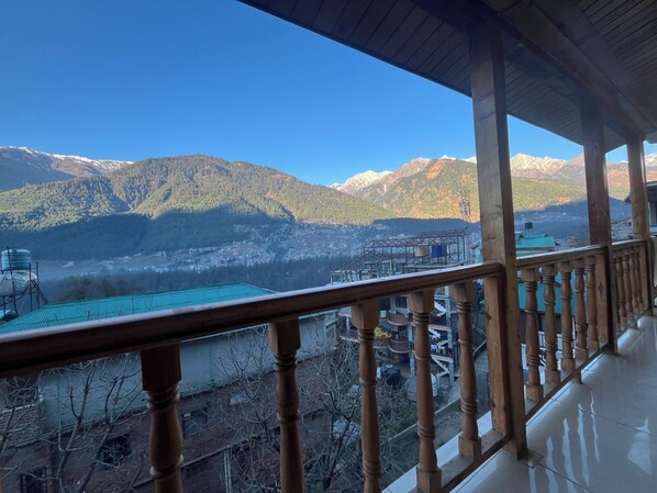 A balcony with a view of a mountainous landscape, a water tower, and a building with a green roof. - Trippeaze stays (Manali)