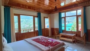 Ein Schlafzimmer mit Holzboden, einem Bett, einem Tisch und zwei Stühlen. Große Fenster bieten Blick auf Grünflächen.