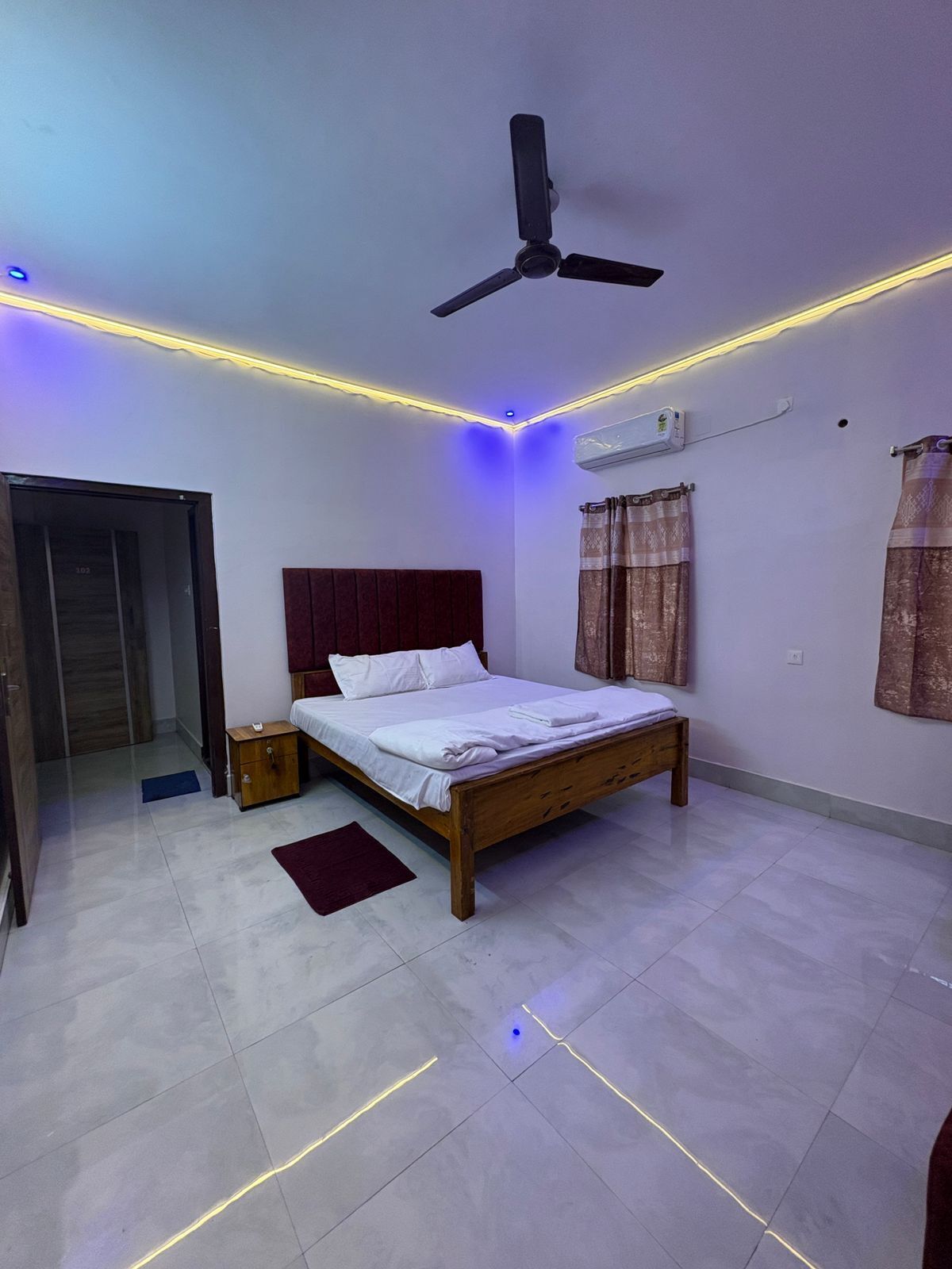 A bedroom with a bed, a ceiling fan, an air conditioning unit, and LED strip lighting along the ceiling.