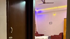 A bedroom with a bed, two red chairs, a ceiling fan, and a wooden cabinet. - Sam Premium  (Bhubaneshwar)