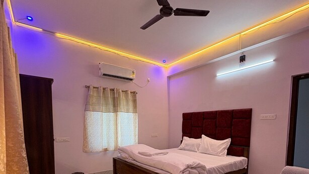 A bedroom with a bed, a ceiling fan, an air conditioning unit, and a window with curtains. - Sam Premium  (Bhubaneshwar)