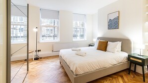 Ett modernt sovrum med en stor säng, två fönster med persienner, ett element och utsikt över staden.