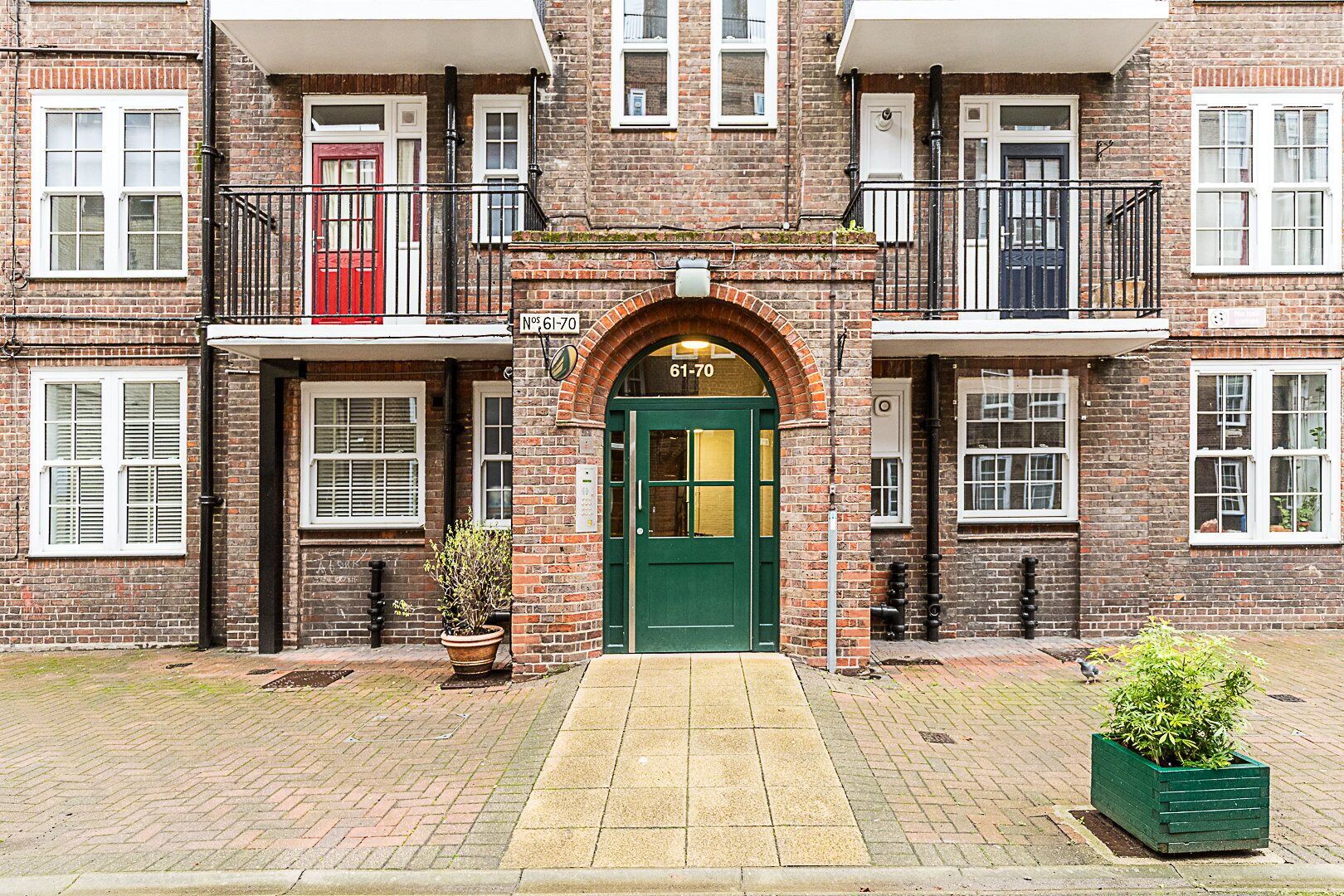 A brick building with a green entrance door, multiple windows, and a small balcony.