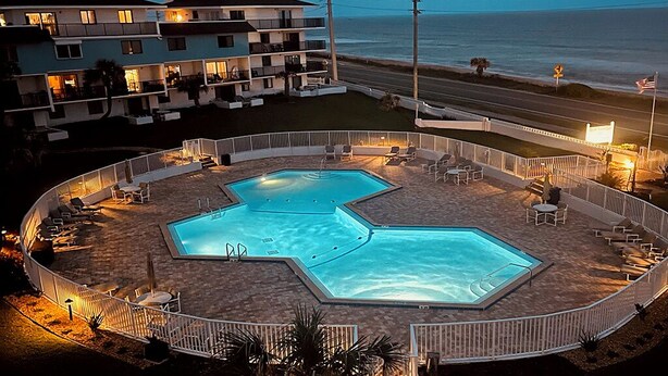 Un hotel con área de piscina que cuenta con dos piscinas, mobiliario exterior y vistas al océano.
