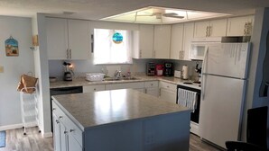 Una cocina con armarios blancos, una isla central, un refrigerador y una cafetera.