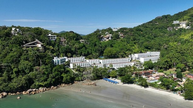 Un hotel costero con vistas a la playa, rodeado de exuberante vegetación y colinas.