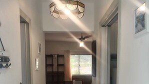 Un pasillo que lleva a un dormitorio con una cama, un ventilador de techo y una ventana con cortinas.