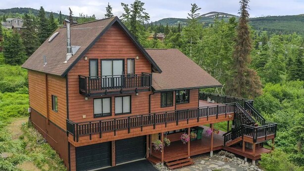 A two-story wooden cabin with a balcony and a stone-paved driveway. - Hillside Haven Anchorage (Anchorage)