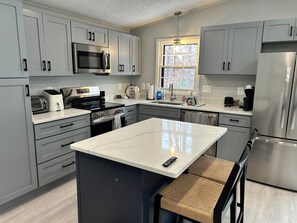A modern kitchen with grey cabinets, stainless steel appliances, a central island with a bench, and a window providing natural light.