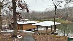 A wooden dock with a covered seating area extending over a lake, surrounded by trees and a path leading to a building. - Bluewater Lake Cabin (Mineral)
