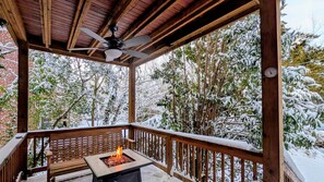 A covered outdoor area with a fire pit and wooden bench, surrounded by snow-covered trees. - Carytown Garden Retreat (Richmond)