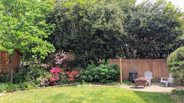 A backyard with a wooden fence, a brick structure, and a lawn. - Carytown Garden Retreat (Richmond)