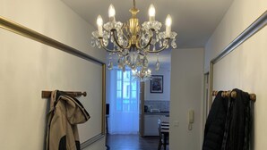 Un couloir orné d’un lustre, muni d’un porte-manteau et d’une porte donnant sur une cuisine.