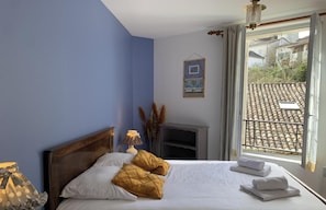 A bedroom with a bed, pillows, a lamp, a window with a view, and a wall-mounted picture. - POTERNE Logement raffiné avec jardin (Aubeterre-sur-Dronne)