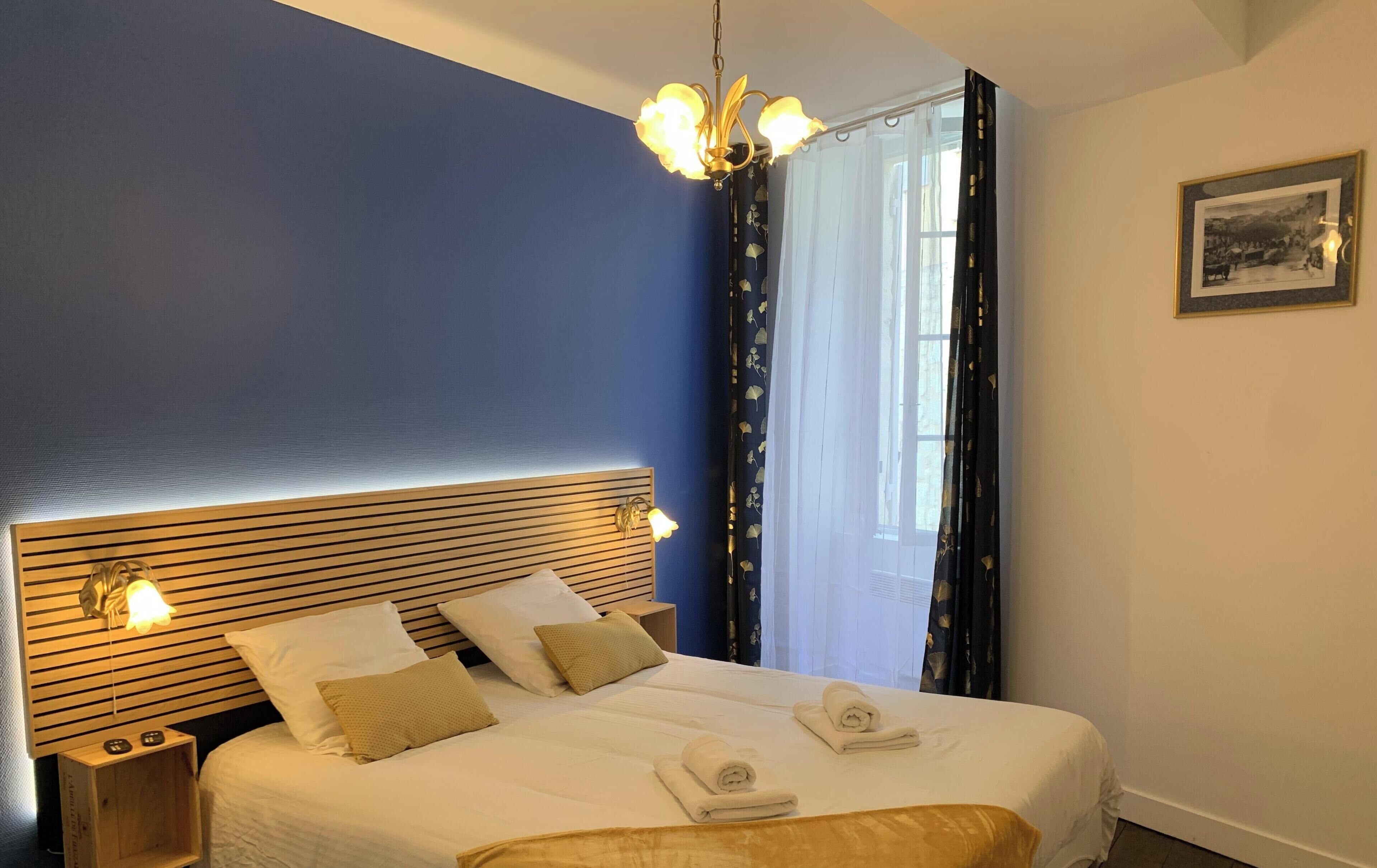 Une chambre d’hôtel avec un grand lit, une tête de lit en bois, deux lampes de chevet et une fenêtre avec des rideaux.