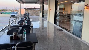 An outdoor dining area with tables and chairs, a covered walkway, and a view of a parking lot. - Jodhana Raj Hotel & Restaurant (Ajmer)