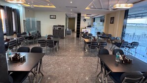 A modern hotel dining area with multiple tables and chairs, a reception desk, and a view of the sea through large windows. - Jodhana Raj Hotel & Restaurant (Ajmer)