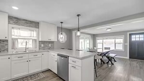 A modern kitchen with white cabinets, a dishwasher, and a dining area with a table and chairs. - Peaceful 3-bedroom cottage on the lake (Trufant)