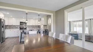 A modern kitchen with white cabinets, a large wooden dining table, and a view through glass doors to a balcony. - Peaceful 3-bedroom cottage on the lake (Trufant)
