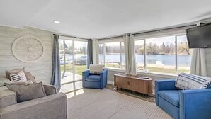 A spacious living room with a large window overlooking a lake, a blue sofa, a grey sofa, and a wooden cabinet. - Peaceful 3-bedroom cottage on the lake (Trufant)