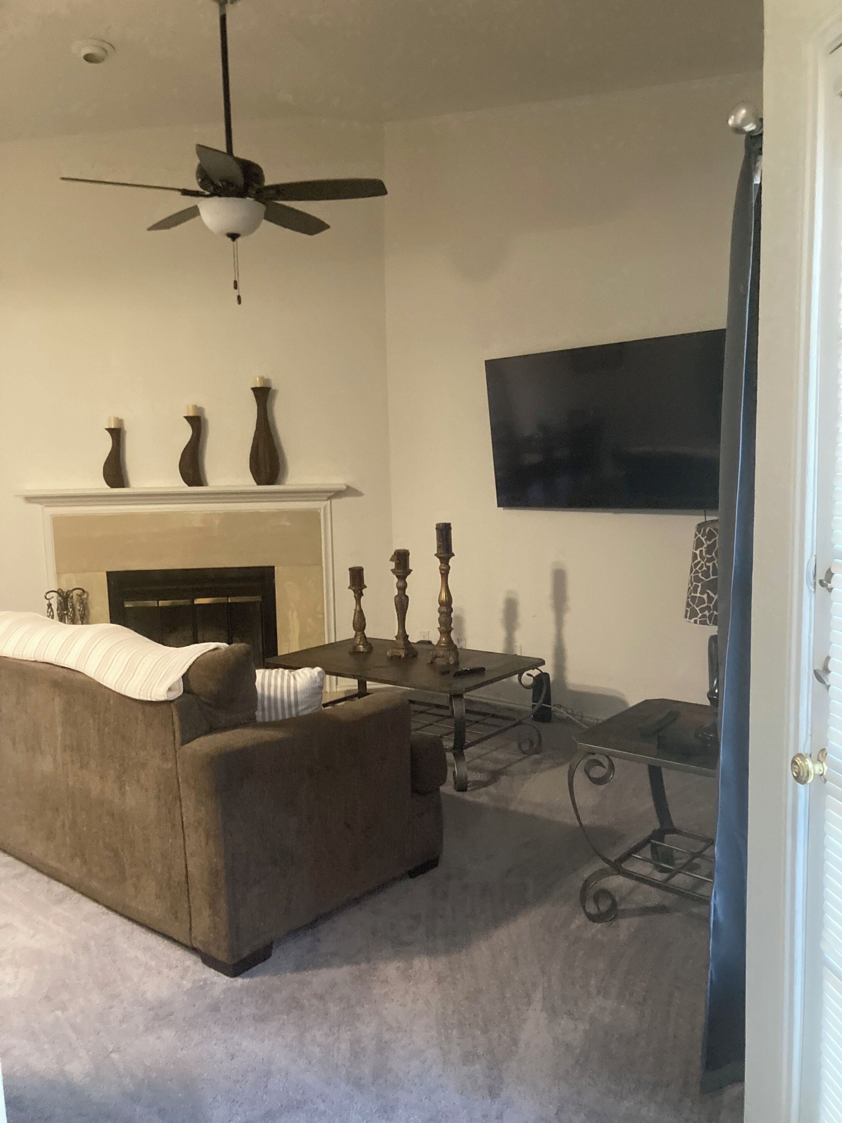 A living room with a sofa, a fireplace, a ceiling fan, and a flat-screen TV mounted on the wall.