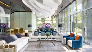 A modern hotel lobby with a central seating area, large windows, and a ceiling with unique lighting fixtures. - New City Condo in Central Bangkok Siam Paragon · Central World (Bangkok)