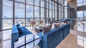 A spacious lounge with large windows, a blue sofa, and a glass coffee table. - New City Condo in Central Bangkok Siam Paragon · Central World (Bangkok)