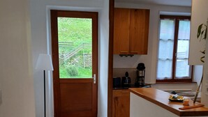 A modern kitchen with wooden cabinets, a coffee maker, and a view of a green garden through a door.