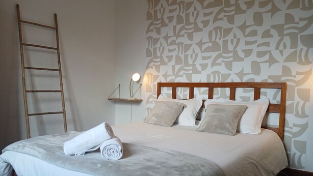 A neatly made bed with a wooden headboard, a bedside lamp, and a wall with a geometric pattern.