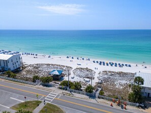 A beach with a building adjacent to the road, a lifeguard tower, and a clear view of the ocean. - White Shores, Pet Friendly, Beautiful massive Pool, Short walk to the Beach. (Miramar Beach)