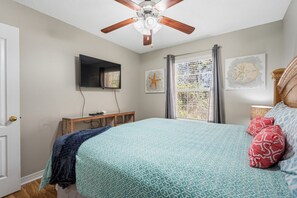 Ein Schlafzimmer mit einem Bett, einem Deckenventilator, einem an der Wand montierten Fernseher und Wandbildern.