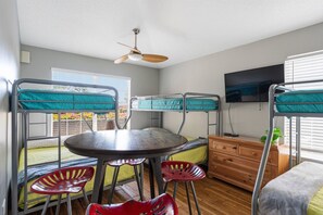 Une petite pièce avec des lits superposés, une table ronde et un ventilateur de plafond.