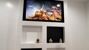 En väggmonterad tv ovanför en vit hylla med dekorativa föremål.