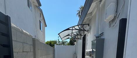 A narrow concrete pathway between buildings with a white exterior and a metal gate on the left.