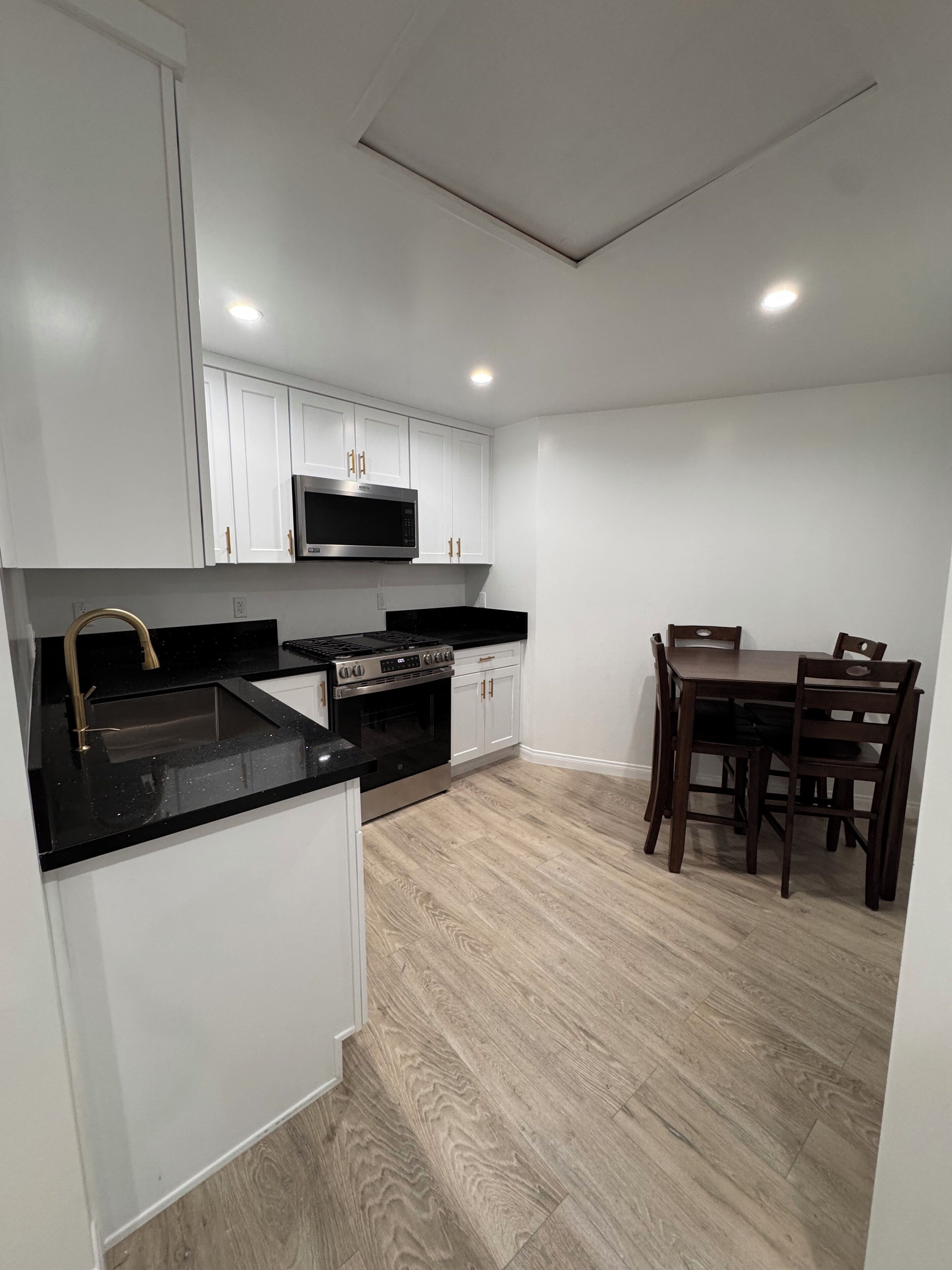 A modern kitchen with white cabinetry, a black countertop, a built-in microwave, and a dining area with a wooden table and chairs.