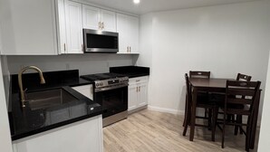Ett modernt kök med vita skåp, en svart bänkskiva, en inbyggd mikrovågsugn och en matplats med ett träbord och stolar.
