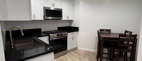 A modern kitchen with white cabinetry, a black countertop, a built-in microwave, and a dining area with a wooden table and chairs.