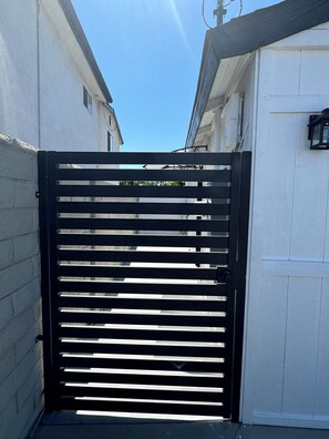 A black metal gate with horizontal slats, white walls, and a clear blue sky. - Cozy 1-bedroom house in peaceful Los Angeles with AC (Los Angeles)