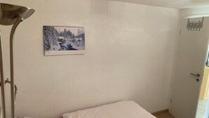 A small, simple room with a single bed, a bedside lamp, and a framed picture on the wall.