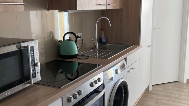 A compact kitchen with a microwave, kettle, stove, and washing machine.