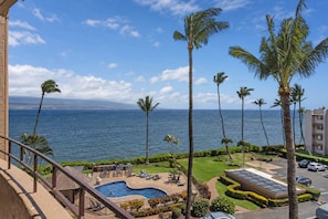 A pool area with a view of the ocean, palm trees, and a building with a parking lot. - Island Sands 500, Breathtaking Ocean Views, Spacious Lanais, Renovated, Split AC (Wailuku)