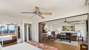 Ein Hotelzimmer mit einem großen Bett, einem Deckenventilator, einem Essbereich mit Tisch und Stühlen, einer Couch und einem Wandbild.