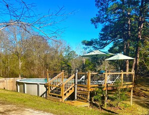Ein Garten mit Whirlpool, Holzterrasse und einem Pavillon mit Sonnenschirm.
