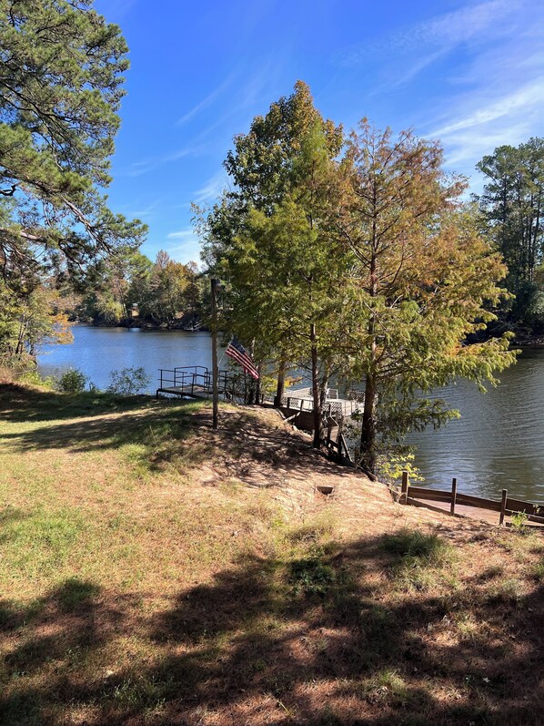 Un parque junto al lago con una pasarela de madera, una bandera y una zona verde.