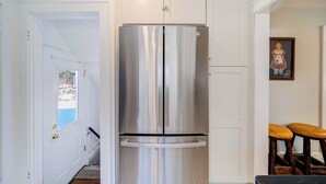 Un réfrigérateur en acier inoxydable dans une cuisine aux armoires blanches, avec un petit tabouret près de la porte.