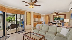 Amplia sala de estar con sofá, mesa de centro y ventiladores de techo. Unos puertas corredizas de vidrio dan a un patio exterior con mobiliario.