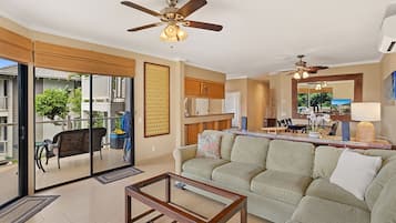 A spacious living room with a sofa, coffee table, and ceiling fans. A sliding glass door leads to an outdoor patio with furniture.